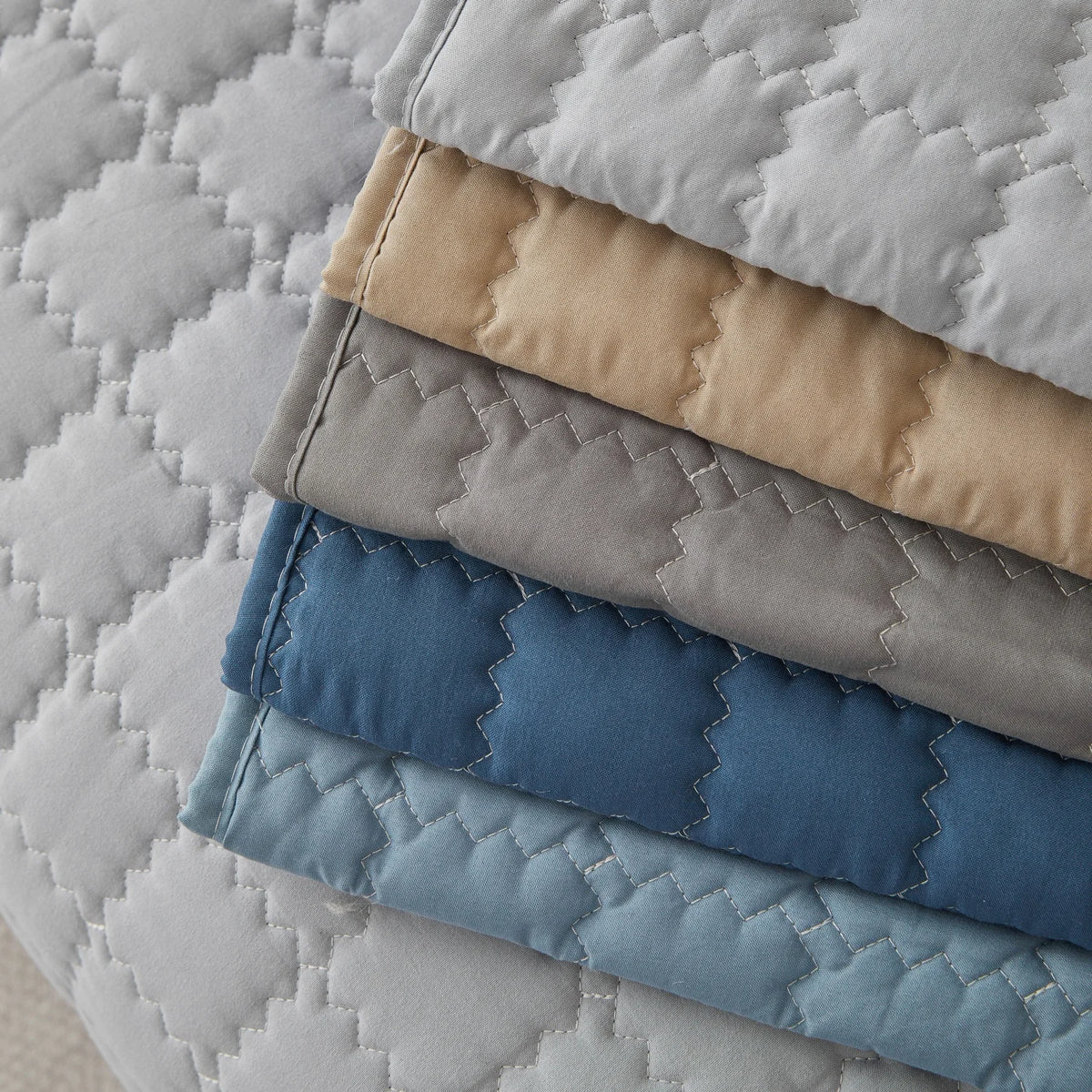 A stack of quilted anti-slip sofa covers in various shades of beige, gray, and blue.