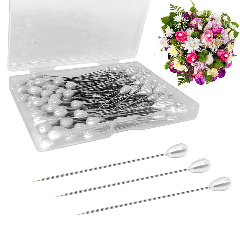 A clear plastic box containing pearl teardrop corsage boutonniere pins and several individual silver-tipped pins.