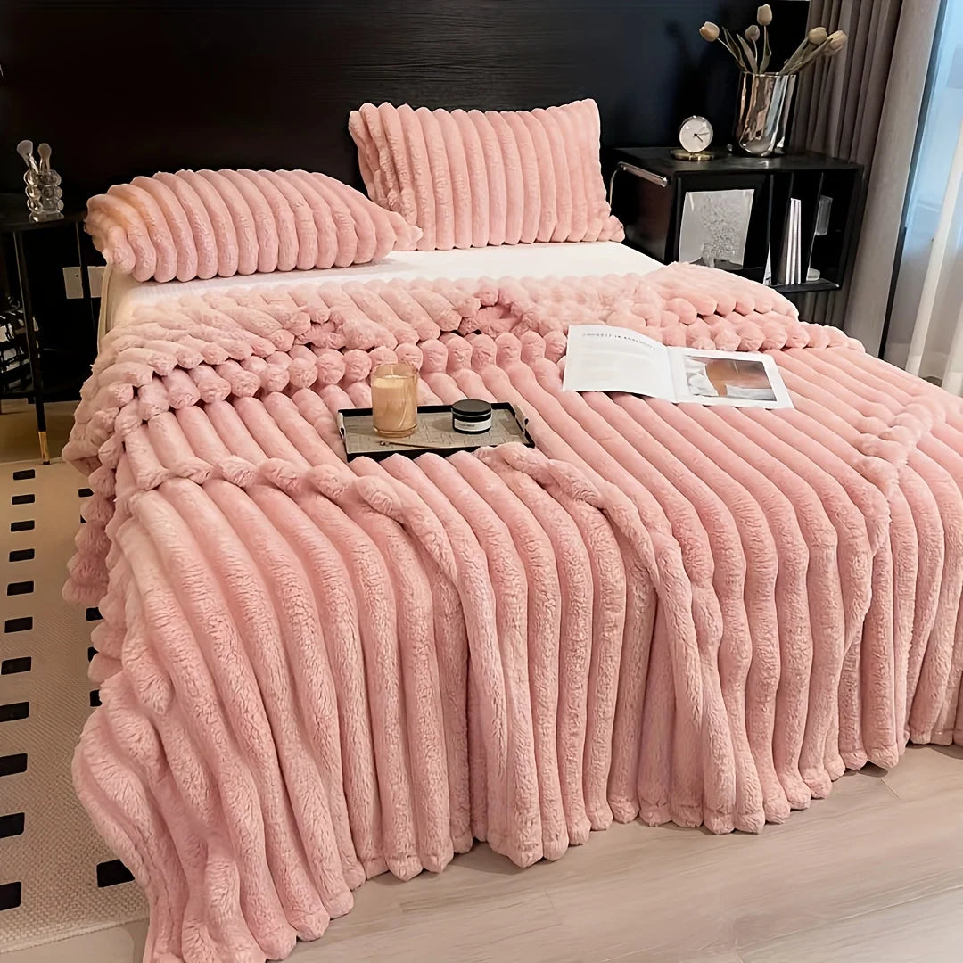 A thick pink fluffy blanket with vertical stripes is displayed on a bed, featuring matching pillows and a throw.