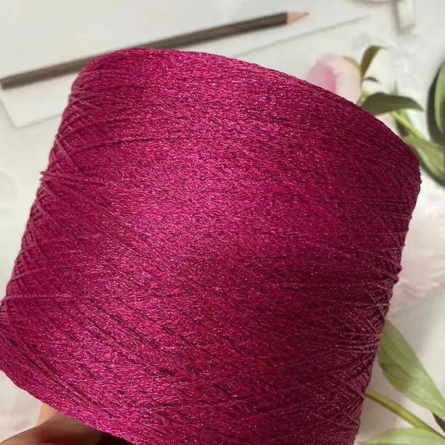 A close-up of vibrant magenta glitter metallic yarn wound into a skein.