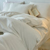 A white 100% cotton yarn-dyed duvet cover with pillows and an open book on a bed.