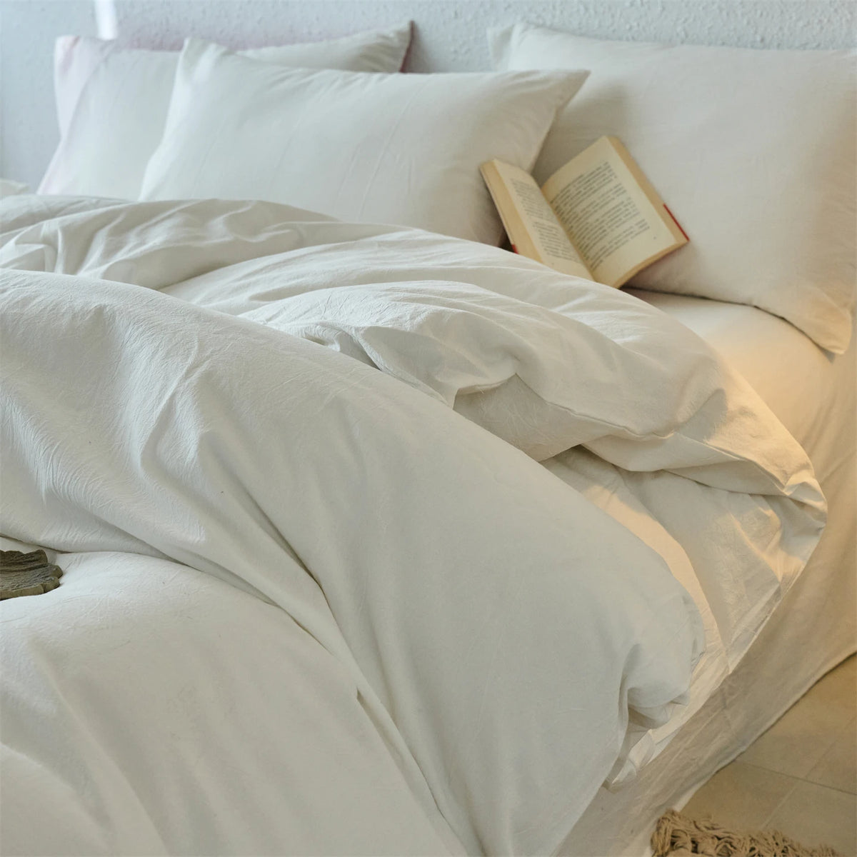 A white 100% cotton yarn-dyed duvet cover with pillows and an open book on a bed.