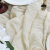 A close-up of a cream semi-sheer gauze table runner draped over a white plate with gold utensils.