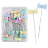 A clear plastic box containing numerous nickel-plated dressmaking pins with colorful butterfly heads.