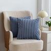 A navy blue faux fur stripe decorative throw pillow resting on a beige upholstered chair.