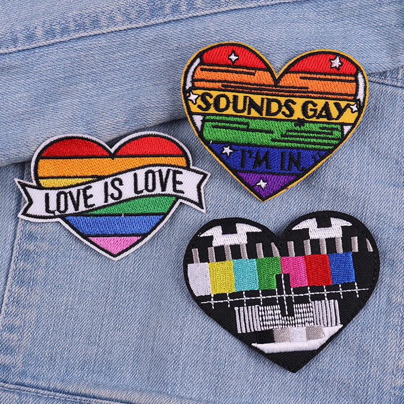 Three heart-shaped embroidered patches featuring rainbow colors and text like Sounds Gay I'm In and Love Is Love