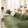 A modern, olive green stretchable elastic sofa cover with a ribbed texture is shown in a bright living room setting.