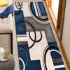 A geometric patchwork floor mat featuring shades of blue, gray, and cream stripes and circular patterns.