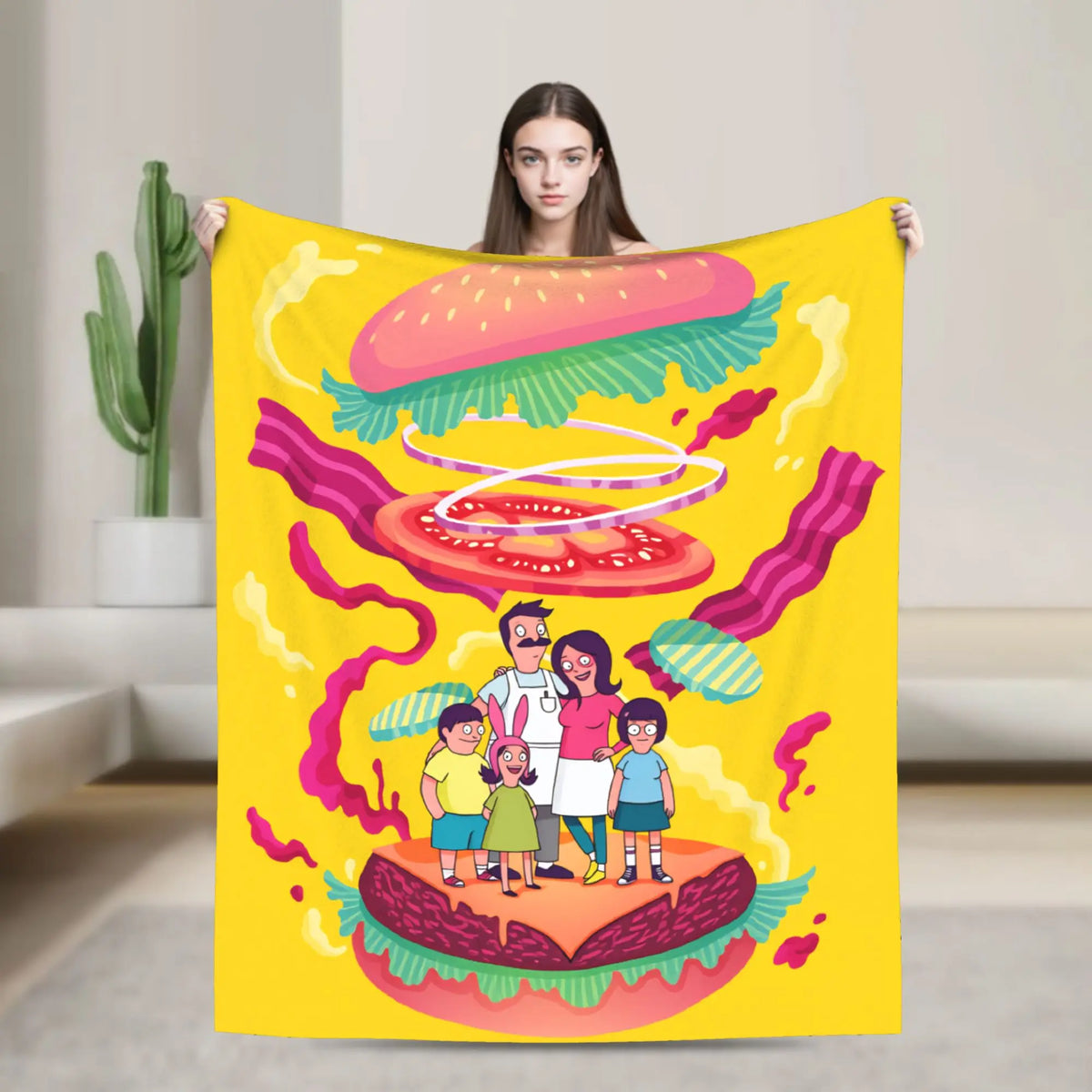 A yellow throw blanket featuring a cartoon illustration of a hamburger and a family standing on the bun.