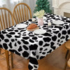 A black and white cow print disposable plastic tablecloth covering a dining table set for a meal.