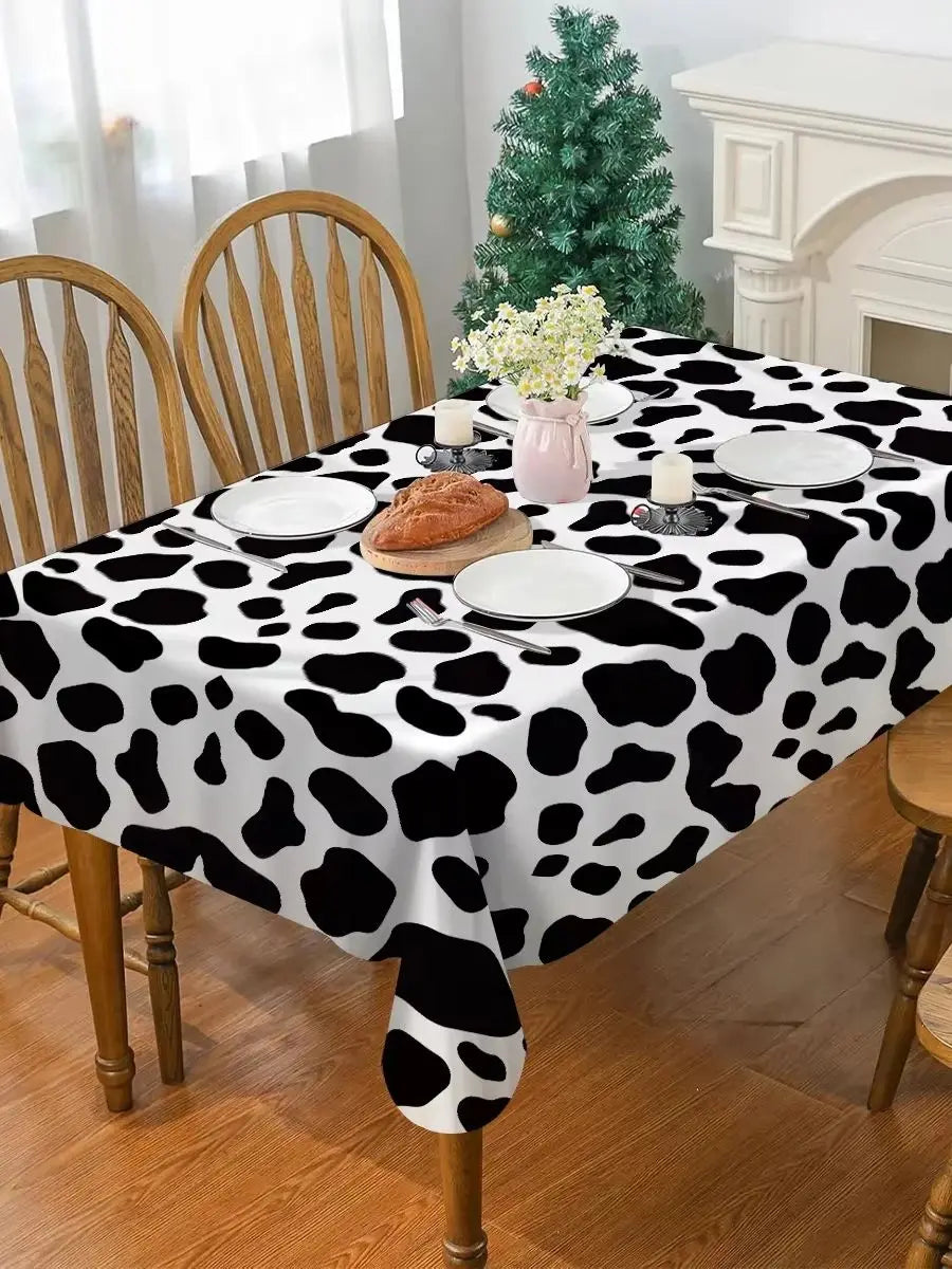 A black and white cow print disposable plastic tablecloth covering a dining table set for a meal.