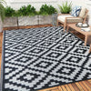 A black and white geometric outdoor rug placed on a wooden deck with greenery in the background.