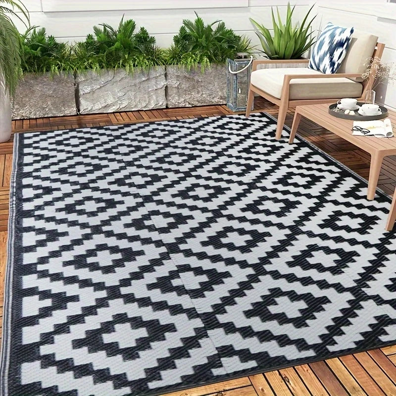 A black and white geometric outdoor rug placed on a wooden deck with greenery in the background.