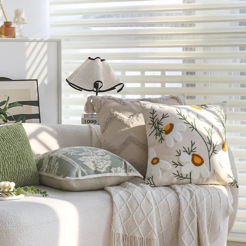A collection of embroidered floral cushion covers and a lampshade displayed on a light-colored sofa near a window.