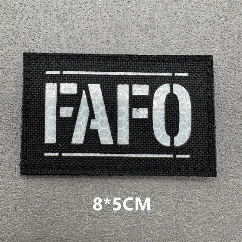 Black embroidered patch with white text FAFO on a gray background
