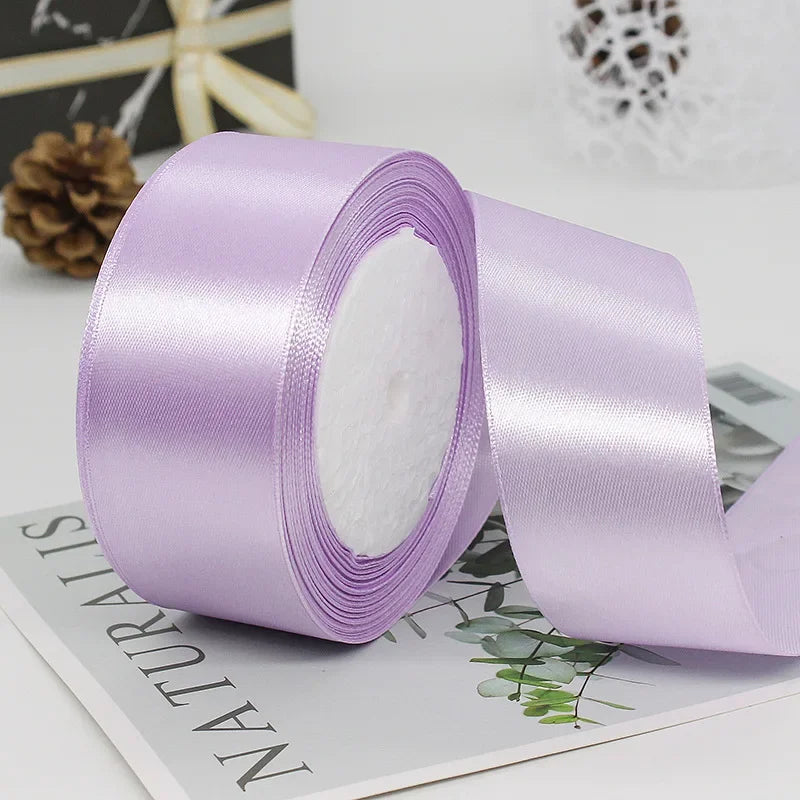 A roll of light purple satin craft ribbon with white filling, lying on a piece of paper.