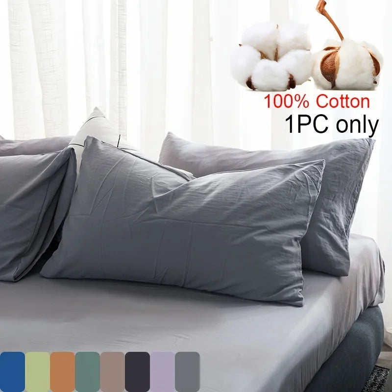Gray cotton pillowcase with white fluffy pom-poms shown on a bed.