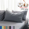 A set of gray cotton pillowcases and decorative pom-pom pillows displayed on a bed.