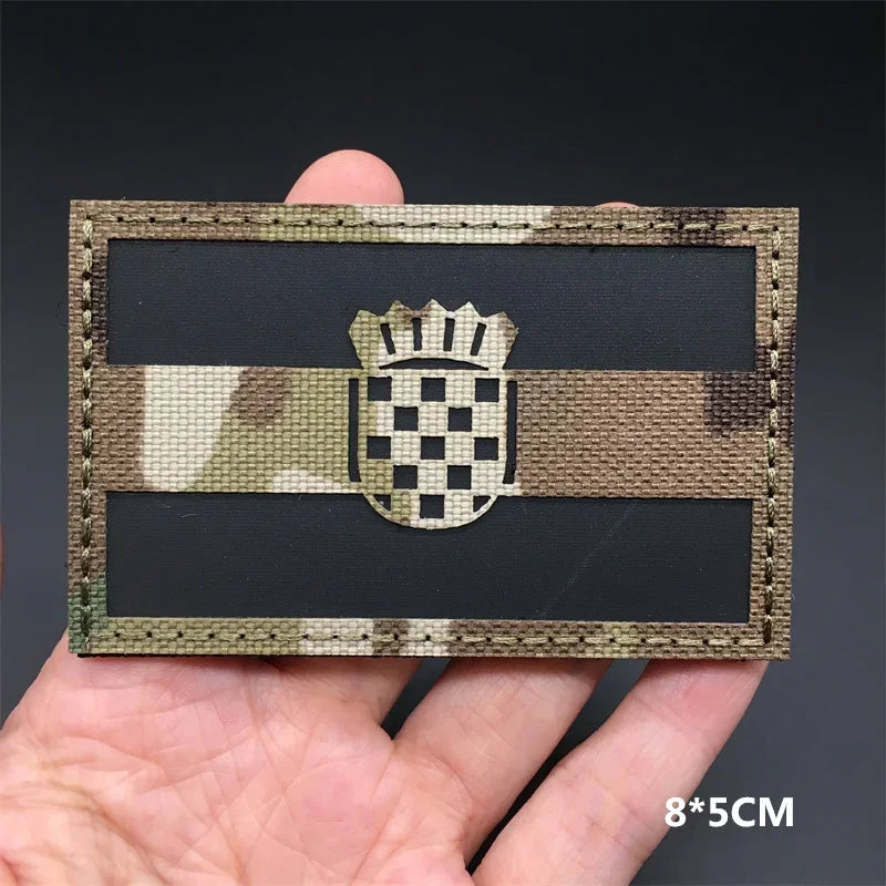 A rectangular tactical flag patch featuring a camouflage background and a central checkered emblem.