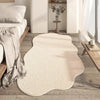 A cream colored irregular plush area rug placed on a light wood floor in a modern living room setting.