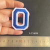 A hand holds a blue and white embroidered iron-on patch shaped like the number zero, measured against a ruler.