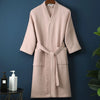 A light pink, textured cotton terry robe is hanging on a dark blue wall.
