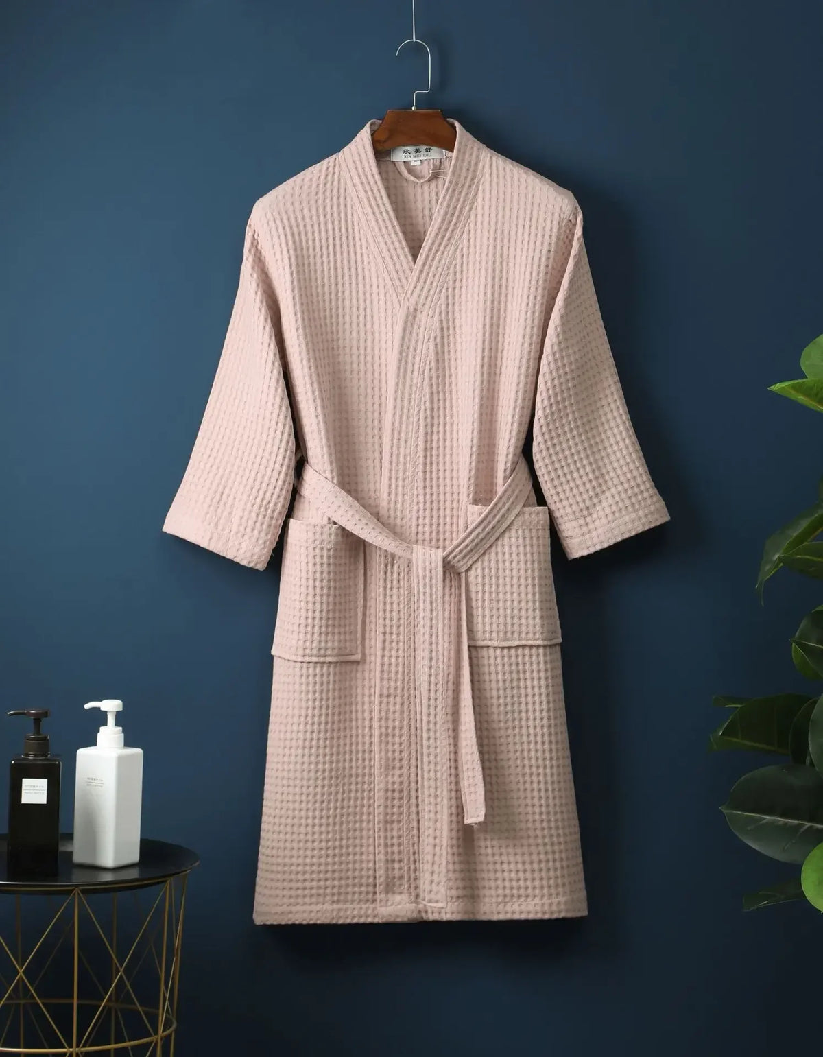 A light pink, textured cotton terry robe is hanging on a dark blue wall.
