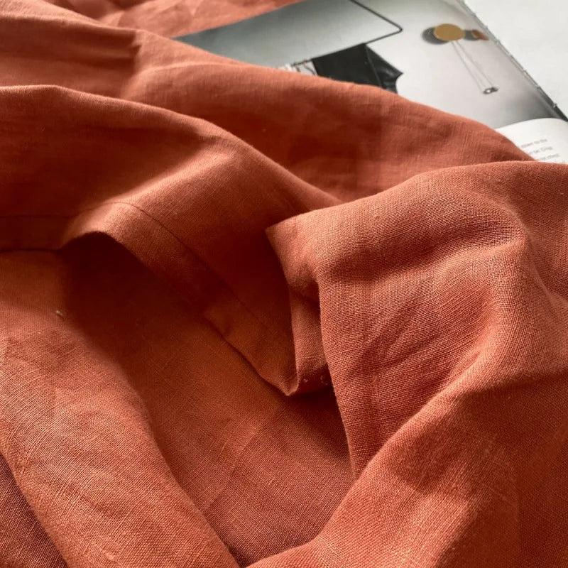 A close-up of a rust orange pure French linen bed sheet fabric draped and folded.