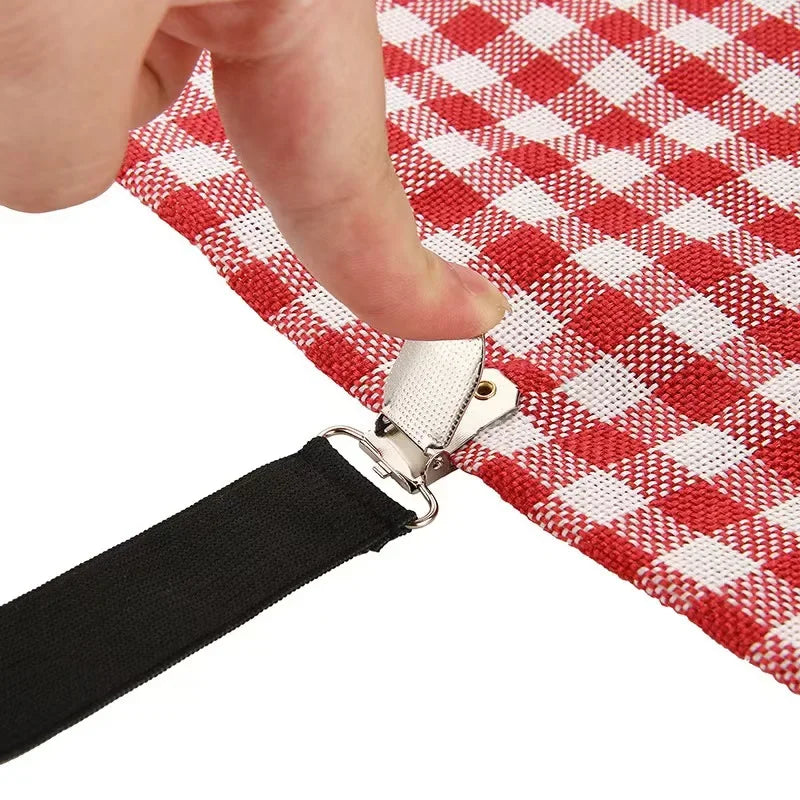 A hand is adjusting an adjustable crisscross bed sheet clip attached to a red and white checkered fabric.