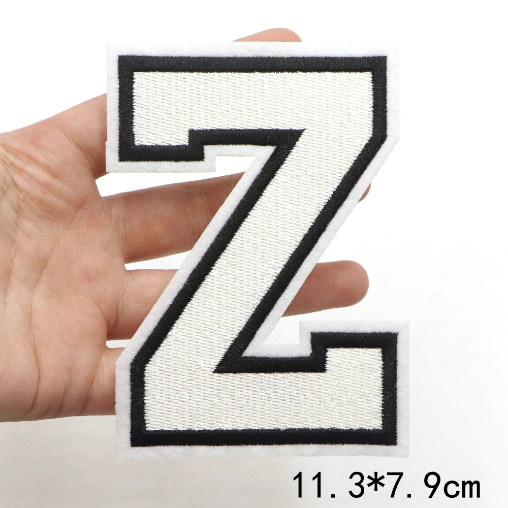 A hand holds a black and white letter Z patch for clothing decoration.