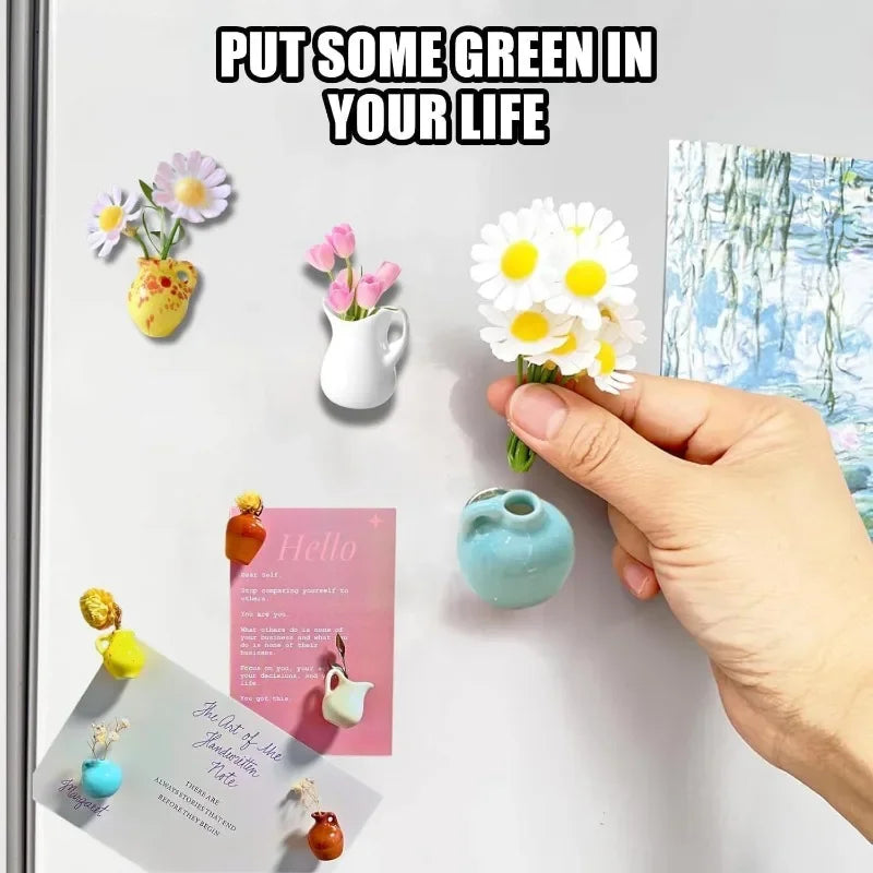 A hand holds a small white ceramic flower magnet next to various colorful floral and landscape magnets on a refrigerator