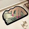 A hand is holding a stack of US dollar bills printed on a black irregular non-slip area rug.