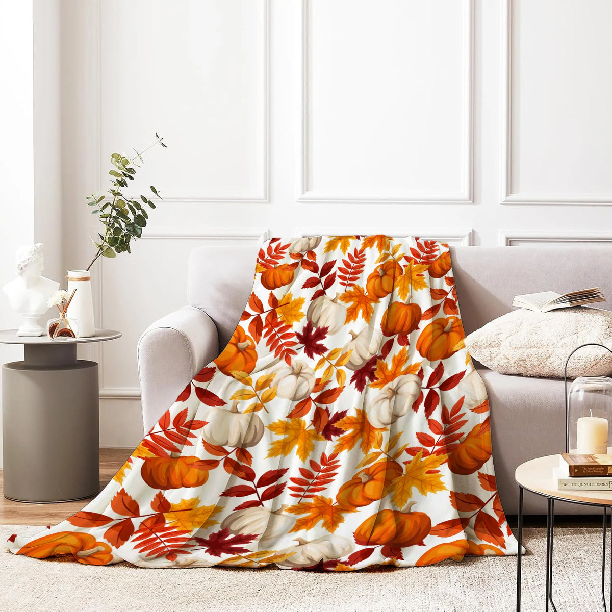 An orange and green flannel throw blanket featuring maple leaf patterns draped over a gray sofa.