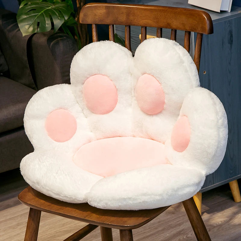 A white plush bear paw cushion resting on a wooden chair.