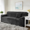 A dark gray stretch velvet sofa slipcover placed on a light rug in a bright room.