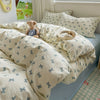 A light beige duvet set with a subtle blue floral pattern is displayed on a bed, featuring matching pillows and a teddy bear.