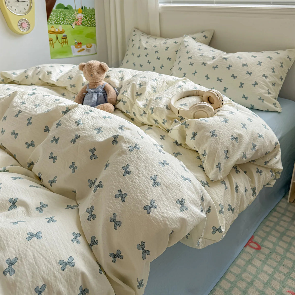 A light beige duvet set with a subtle blue floral pattern is displayed on a bed, featuring matching pillows and a teddy bear.