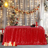 A red sequin rectangle table cover is displayed on a table, decorated with festive string lights and holiday greenery.