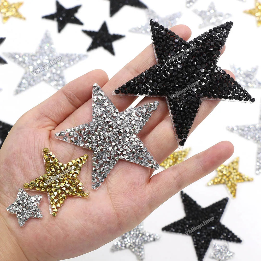 A hand holds several glitter rhinestone star-shaped iron-on patches for clothing.