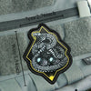 A black and yellow military morale patch featuring a detailed snake design on a gray fabric background.