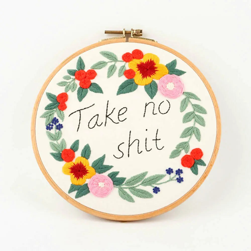 A circular embroidery hoop featuring floral cross stitch embroidery with green leaves and red, yellow, and pink flowers.