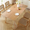 A light wood dining table protected by a clear heat-resistant PVC tablecloth protector with natural wood chairs and floral ce