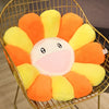 A round, smiling sunflower plush cushion in orange and yellow colors displayed in a gold wire basket.