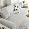 A light gray stretchable sofa cover with white decorative pillows and a small teacup on the fabric.