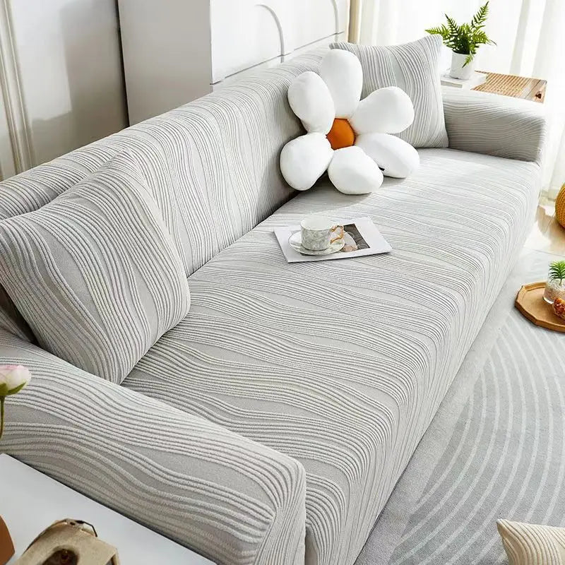A light gray stretchable sofa cover with white decorative pillows and a small teacup on the fabric.