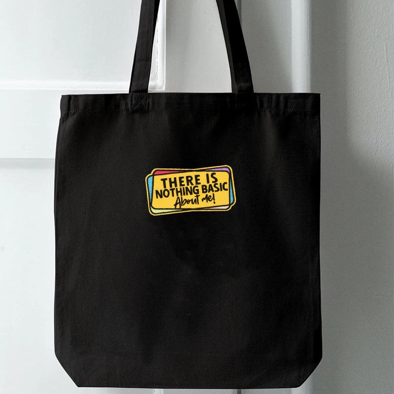 Black tote bag with a yellow and purple embroidered patch that reads There is nothing basic about me