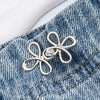 Silver adjustable leaf clover waist tightener attached to blue denim fabric.