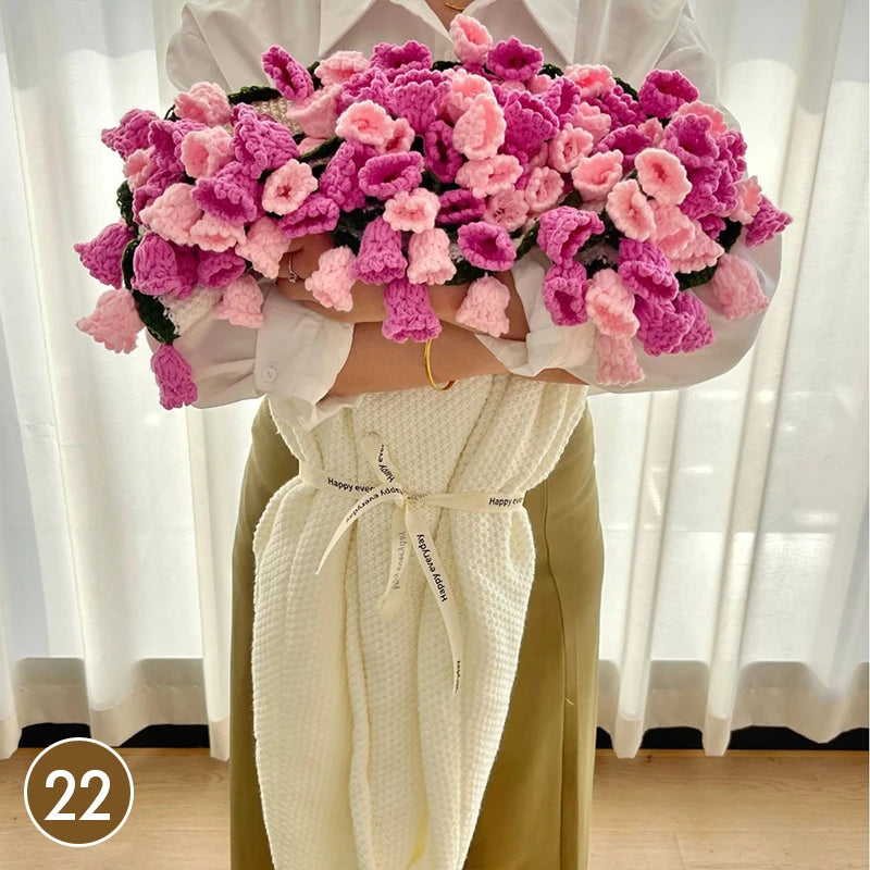 A hand knitted floral rose bouquet throw blanket in shades of pink and purple is displayed against a white background.