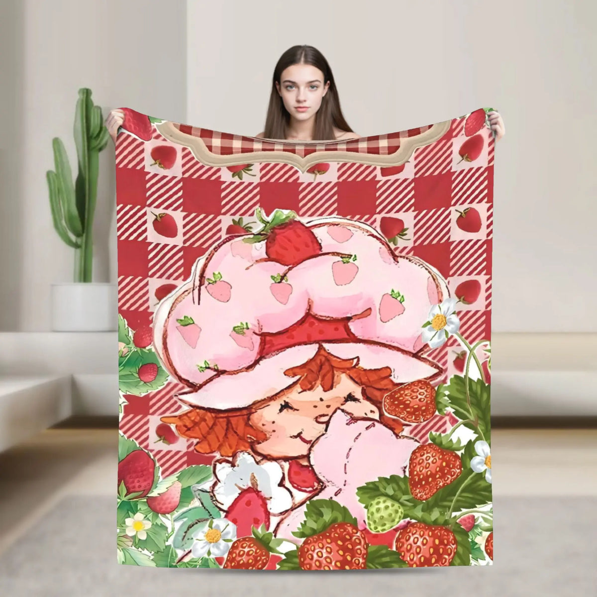 A strawberry shortcake plush throw blanket featuring a pink strawberry character and red checkered fabric.