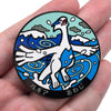 A round metal brooch pin featuring a white divine beast design with blue accents on a teal background.